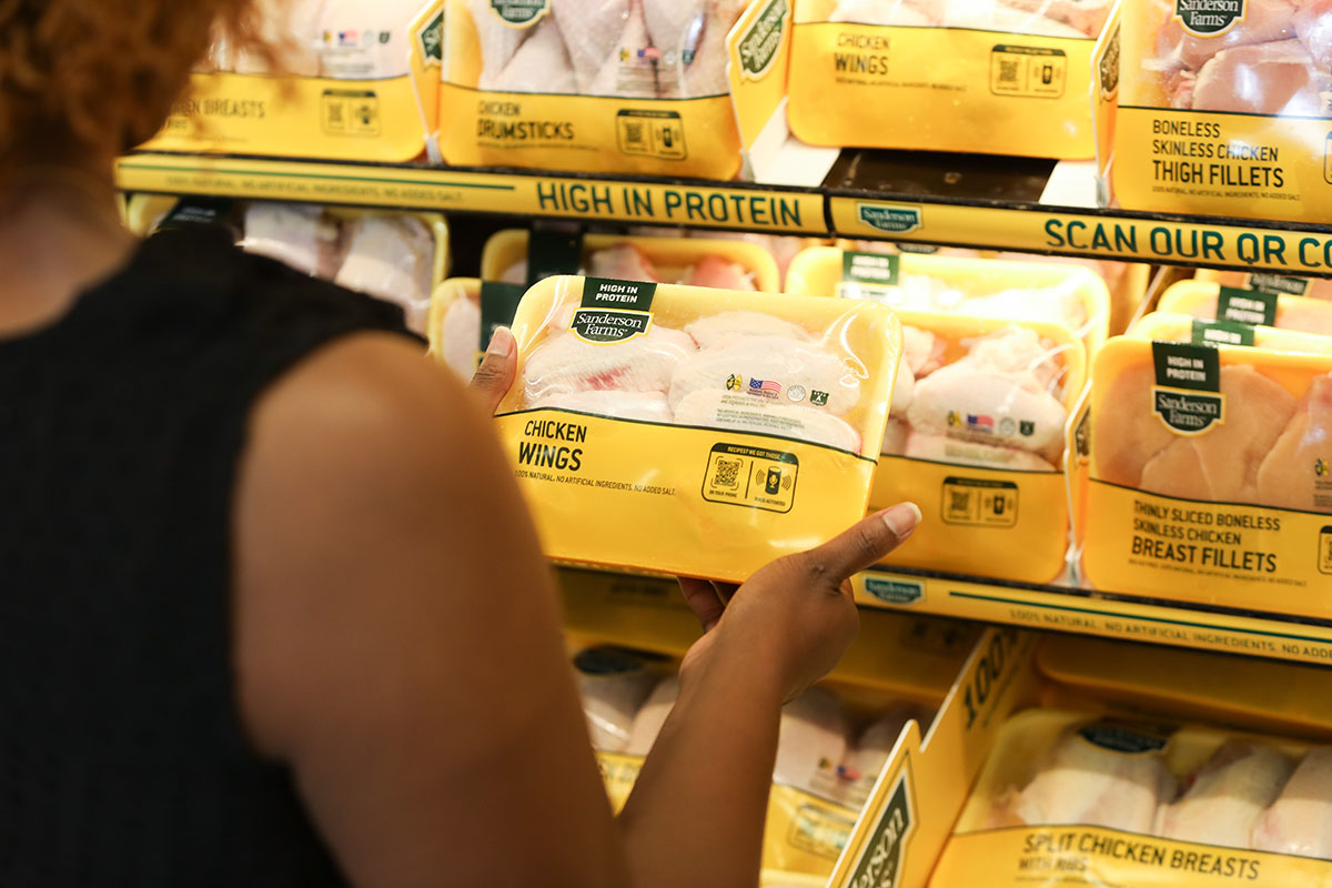 woman looking at a package of chicken at a store