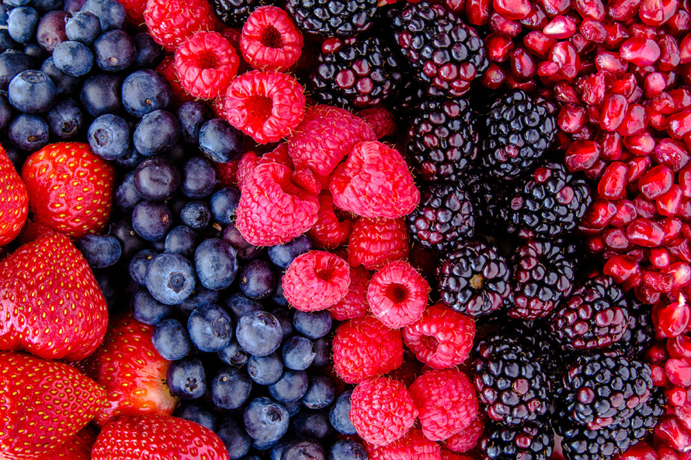 Fresh organic pomegranate seeds, blackberries, raspberries, blueberries and strawberries in lines next to each other