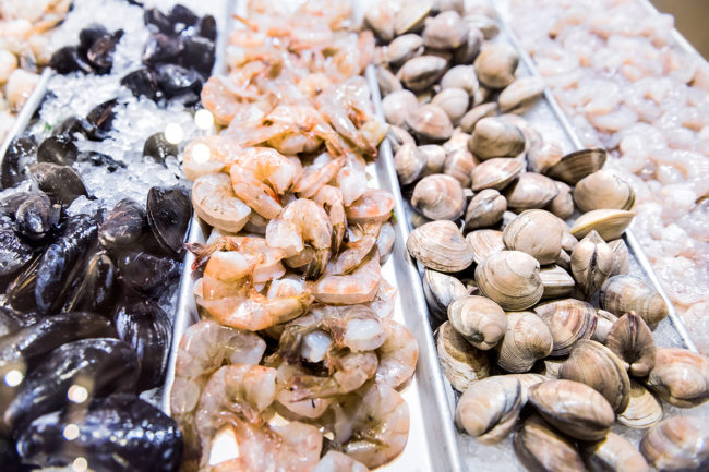 Large raw green clams shells mussels closeup shrimp crustacean prawns seafood stand on ice in fresh market behind glass on display in store, shop